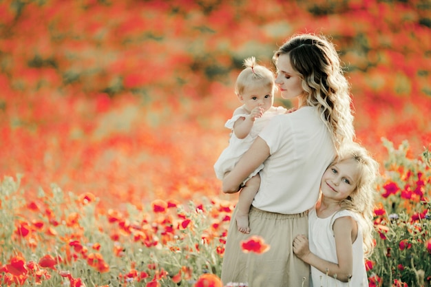 Mutter sieht ihr Baby an, ältere Tochter schmiegt sich an Mutter auf dem Mohnblumenfeld