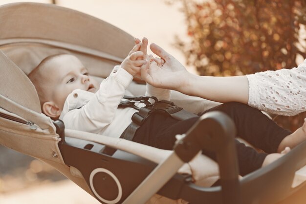 Mutter trägt Gesichtsmaske. Frau sitzt auf einer Bank. Mutter mit Kinderwagen während der Pandemie, die einen Spaziergang im Freien macht.