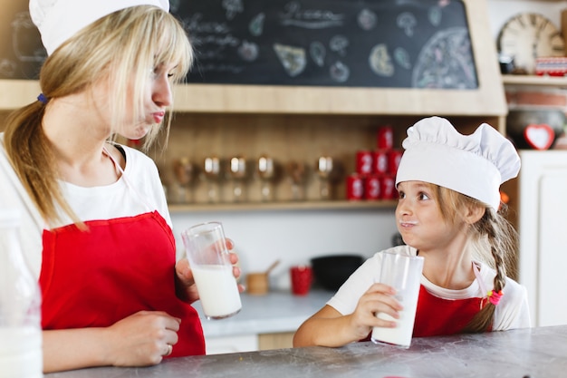 Mutter und charmante kleine Tochter haben Spaß beim Trinken von Milch am Tisch in einer gemütlichen Küche