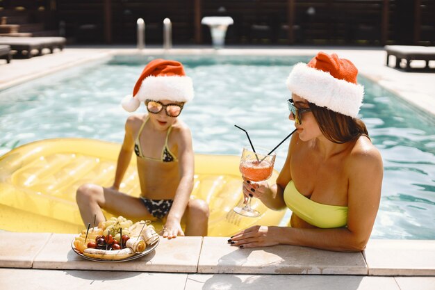 Mutter und ihr Kind in Weihnachtsmützen am Pool. Urlaub im exotischen Land.