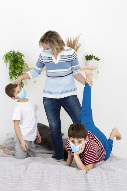 Mutter und Kinder spielen zusammen, während sie medizinische Masken tragen