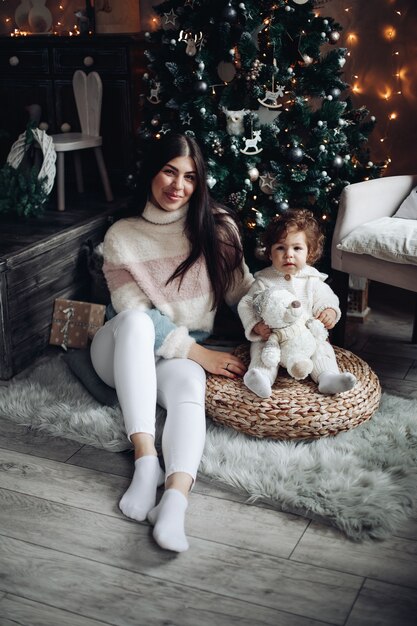 Mutter und kleine süße Tochter sitzen zu Hause neben einem Weihnachtsbaum