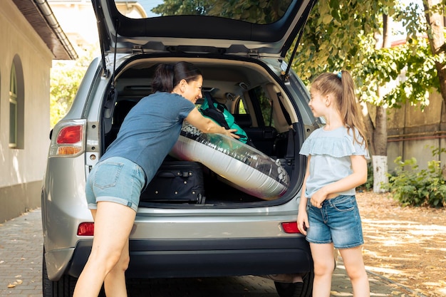 Mutter und kleines Kind laden Gepäck in den Kofferraum, um Urlaub am Meer zu machen. Reisen im Sommer mit Fahrzeug und Gepäck, Koffer, Schlauchboot und Trolley.