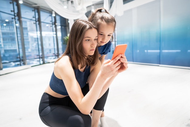 Mutter und Mädchen, die Telefon im Fitnessstudio zum Ansehen des Videos verwenden
