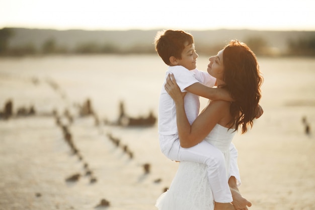 Mutter und Sohn sind in weiße Freizeitkleidung gekleidet und schauen sich bei Sonnenuntergang gegenseitig an