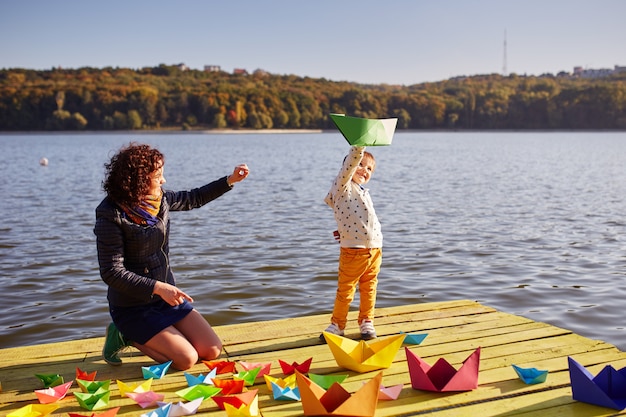 Mutter und Sohn spielen mit Papierbooten am See