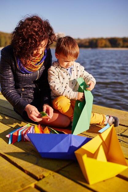 Mutter und Sohn spielen mit Papierbooten am See