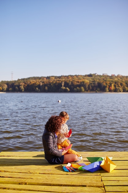 Mutter und Sohn spielen mit Papierbooten am See