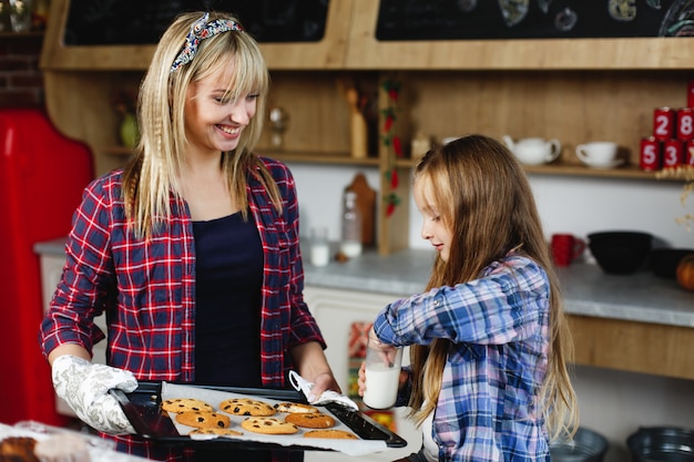 Mutter und Tochter auf einer Küche schmecken frisch gebackene Schokoladenplätzchen mit Milch