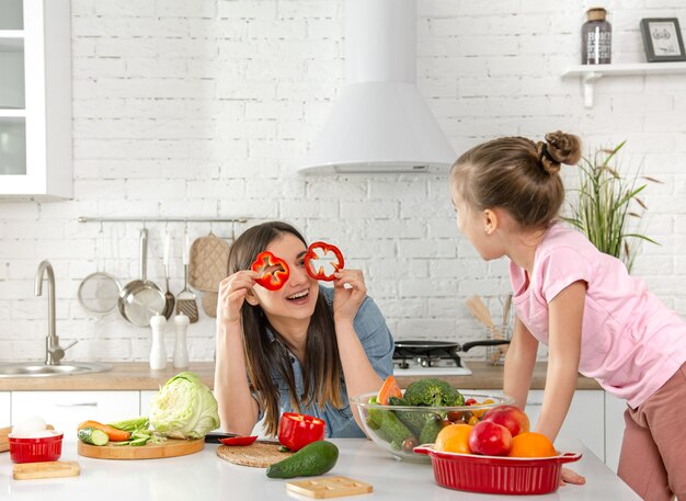 Mutter und Tochter bereiten in der Küche einen Salat zu. Viel Spaß und spielen Sie mit Gemüse. Das Konzept einer gesunden Ernährung und eines gesunden Lebensstils. Deutsche Ernährung und ein gesunder Lebensstil.