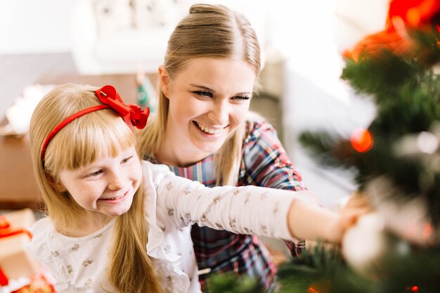 Mutter und Tochter, die zusammen Weihnachtsbaum verzieren