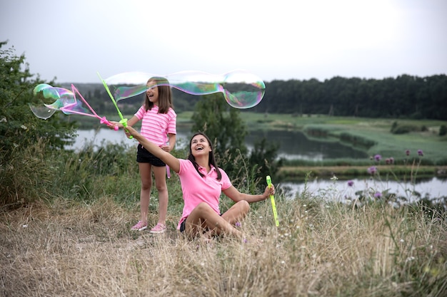 Mutter und Tochter haben Spaß zusammen, machen große Seifenblasen, Erholung im Freien.