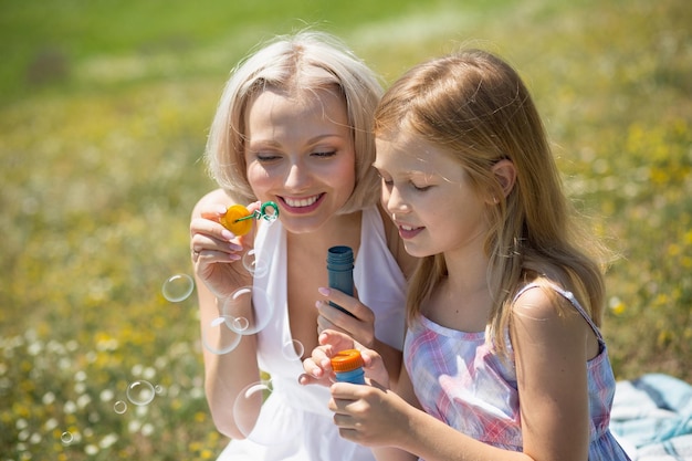 Mutter und Tochter im Freien. Mutter und ihr Kindermädchen spielen mit Blasengebläse.