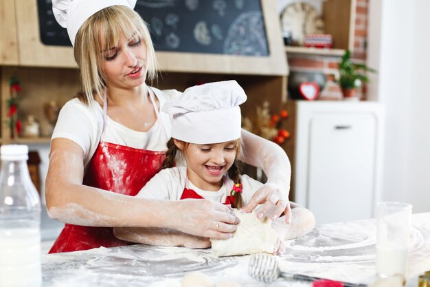 Mutter und Tochter in derselben Kleidung haben Spaß daran, einen Teig in einer gemütlichen Küche zuzubereiten