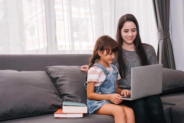 Mutter und Tochter verbringen Zeit zusammen im Wohnzimmer Mutter bringt ihrer Tochter Homeschooling online über Laptop-Remote-Studien-E-Learning bei