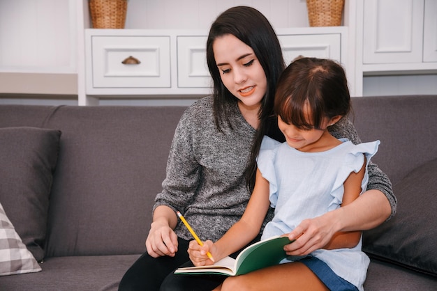 Mutter und Tochter verbringen Zeit zusammen im Wohnzimmer Mutter unterrichtet ihre Tochter im Homeschooling und liest zu Hause ein Buch