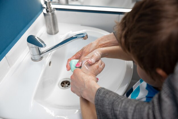 Mutter wäscht Hände ihres Sohnes sorgfältig im Badezimmer Nahaufnahme. Prävention von Infektionen und der Ausbreitung von Lungenentzündungsviren