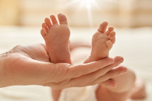 Mutters Hand hält den Barfuß des Neugeborenen, Mama macht Massage für Säugling zur Normalisierung des Nervensystems und Entwicklung der Bewegungskoordination.