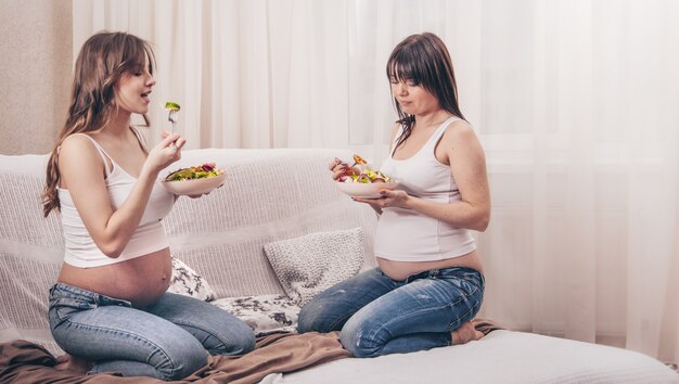 Mutterschaftskonzept, zwei schwangere Frauen, die frischen Salat zu Hause essen