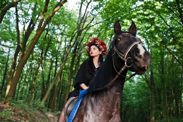 Mystisches Mädchen in Kranzkleidung in Schwarz am Pferd in Holz