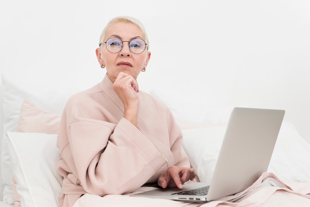 Kostenloses Foto nachdenkliche ältere frau, die im bett mit laptop aufwirft