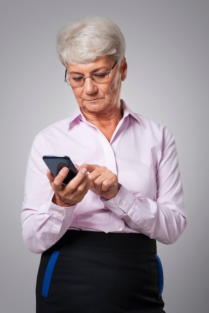 Nachdenkliche ältere Geschäftsfrau, die Smartphone benutzt