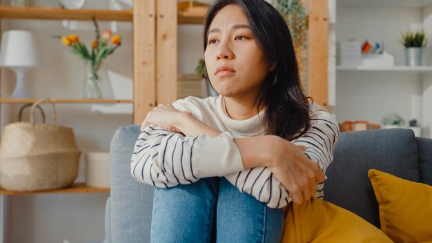 Nachdenkliche asiatische Dame sitzen mit einem Gefühl der Einsamkeit, fühlen sich deprimiert und verbringen Zeit alleine zu Hause zu bleiben