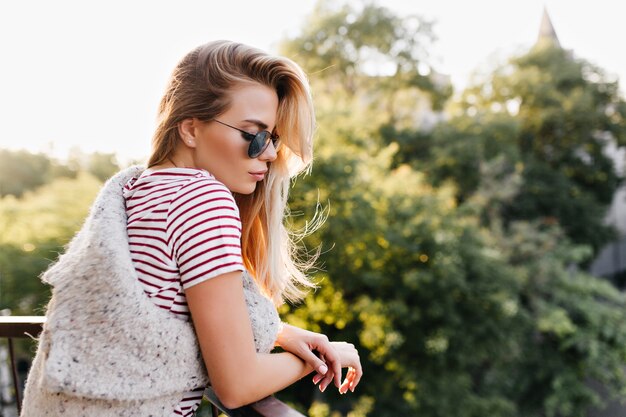 Nachdenkliche europäische Frau in der Sonnenbrille, die Naturblick genießt, während auf Terrasse steht