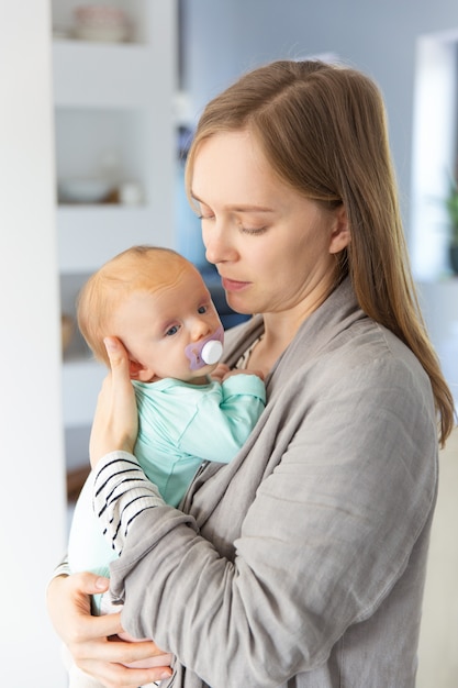 Nachdenkliche fokussierte neue Mutter, die Baby hält