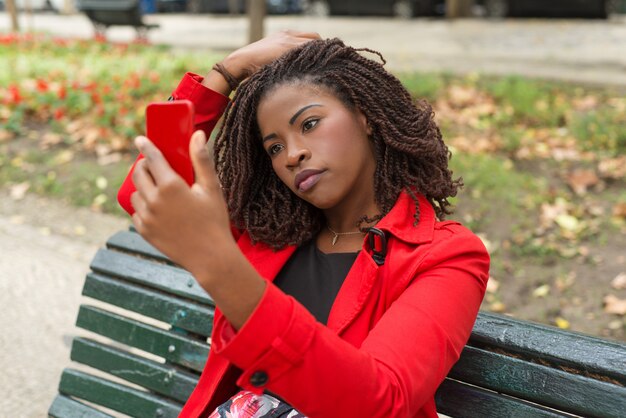 Nachdenkliche Frau, die Smartphone im Park verwendet