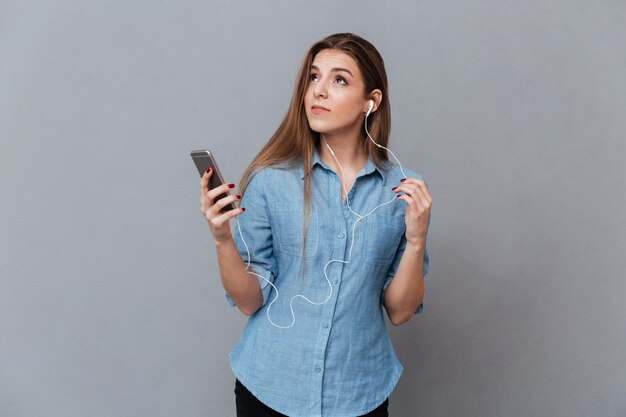 Nachdenkliche Frau im Hemd, die Musik am Telefon hört