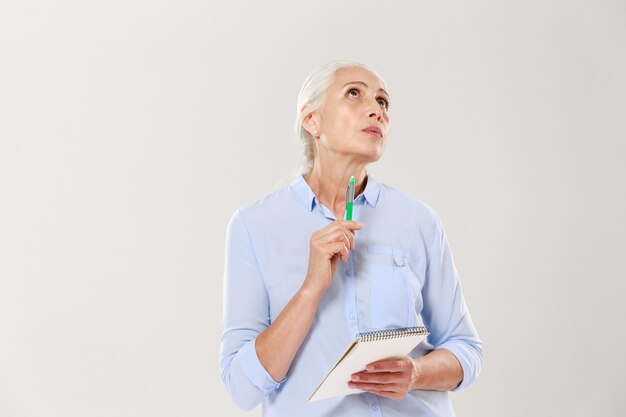 Nachdenkliche Frau mit Notizbuch und Stift, die denken und nachschlagen