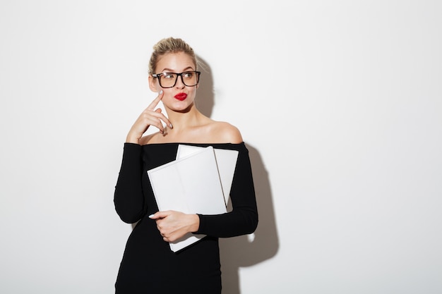 Nachdenkliche Geschäftsfrau im Kleid und in Brillen, die Dokumente verwahren