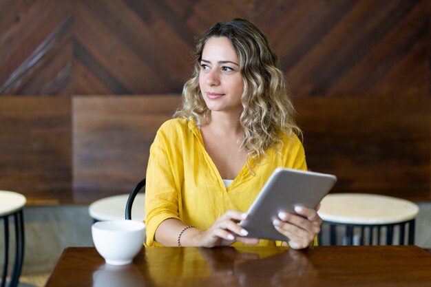 Nachdenkliche hübsche junge Frau, die am Cafétisch mit Tabelle sitzt