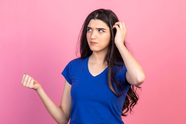 Nachdenkliche junge Dame, die auf rosafarbenem Hintergrund steht und denkt