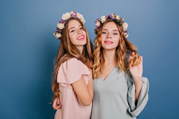 Nachdenkliche junge Dame mit hellem lockigem Haar, das ihre Freundin umarmt