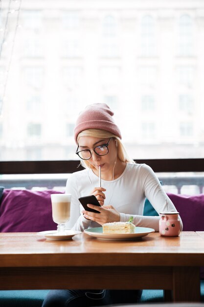 Nachdenkliche junge Frau, die Smartphone im Café isst und benutzt