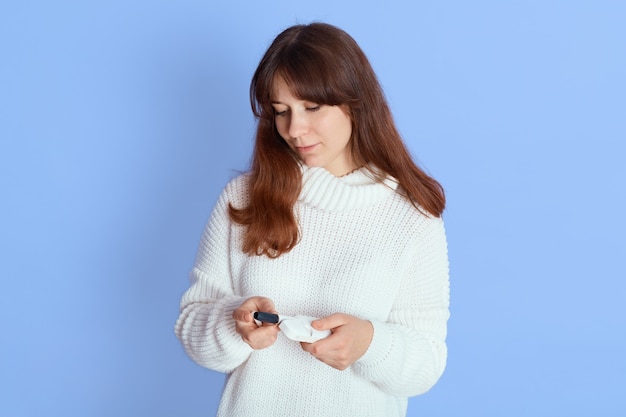 Nachdenkliche junge Frau, die weißen lässigen Strickpullover mit Tabakheizstäben trägt, die über blau, Dame mit elektronischer Zigarette schauen.