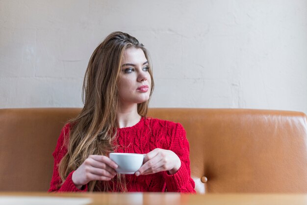 Nachdenkliche junge Frau mit Cup sitzt auf einer Couch