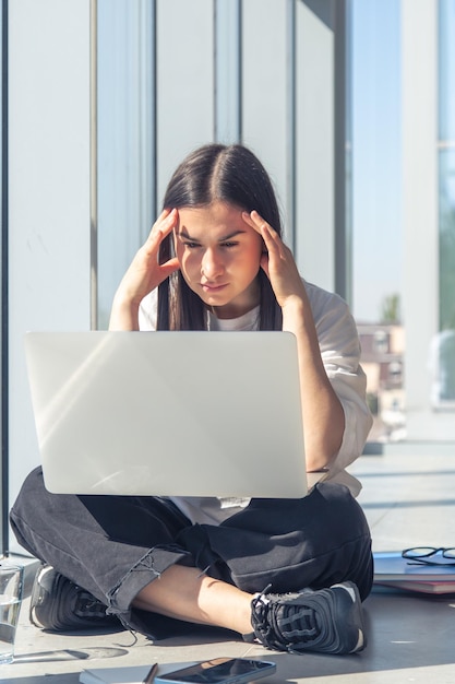 Nachdenkliche junge Frau vor einem Laptop-Bildschirm im Büro am Fenster