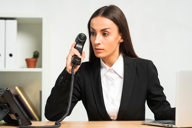 Nachdenkliche junge Geschäftsfrau, die im Büro hält Telefonhörer sitzt