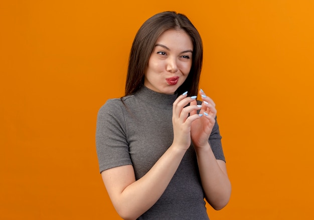 Nachdenkliche junge hübsche Frau, die Hände zusammenhält, die gerade lokal auf orange Hintergrund mit Kopienraum suchen