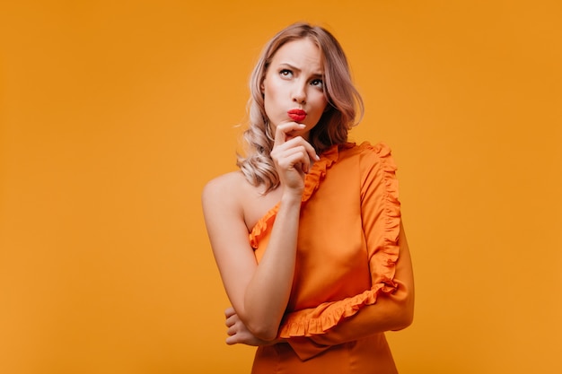 Nachdenkliche lockige Frau im orange Kleid, das oben schaut