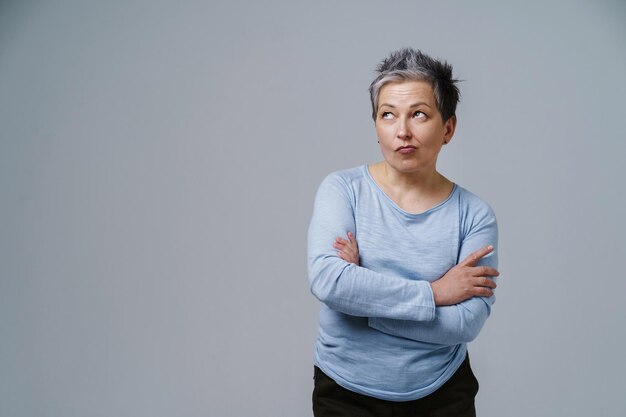 Nachdenkliche, nachdenkliche Zweifel, reife Frau mit grauem Haar in den 50er Jahren, die mit gefalteten Händen posiert und Platz für Kopien auf der linken Seite isoliert auf weißem Hintergrund bietet. Platz für Produktplatzierung. Gealterte Schönheit Getöntes Bild