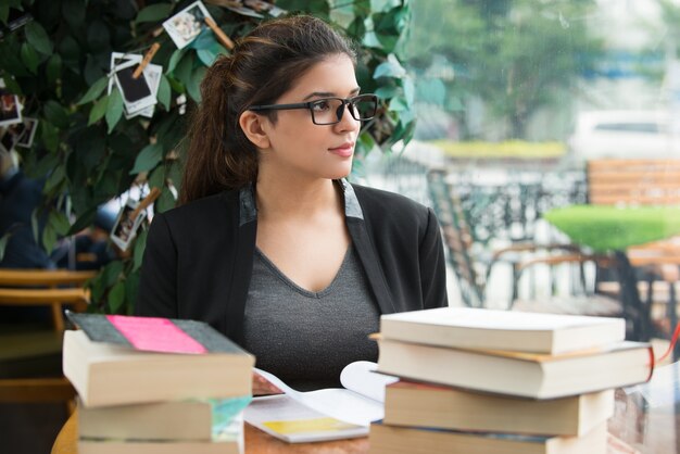 Nachdenkliche Studentin sitzt am Tisch mit Büchern