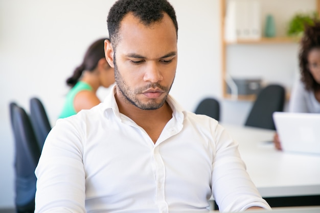 Nachdenklicher Büroangestellter, der bei Tisch sitzt und Laptop betrachtet