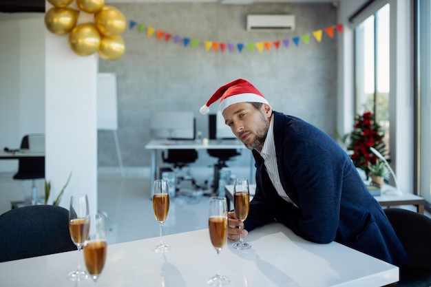 Kostenloses Foto nachdenklicher geschäftsmann, der champagner trinkt, während er allein auf der weihnachtsfeier im büro ist