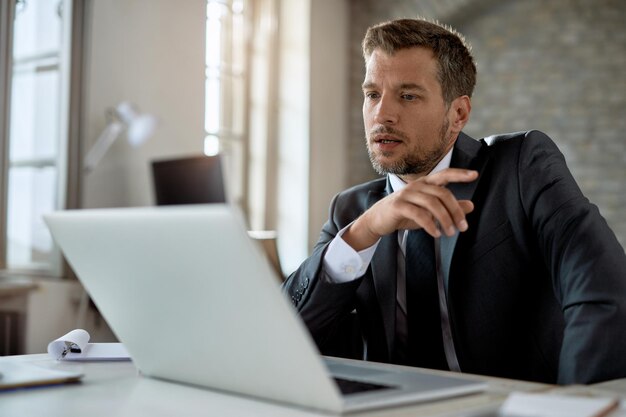 Nachdenklicher Geschäftsmann, der im Büro arbeitet und eine E-Mail auf dem Laptop liest