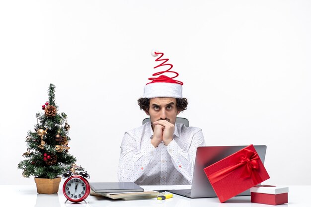 Nachdenklicher junger Geschäftsmann mit lustigem Weihnachtsmannhut, der an etwas im Büro auf weißem Hintergrund denkt