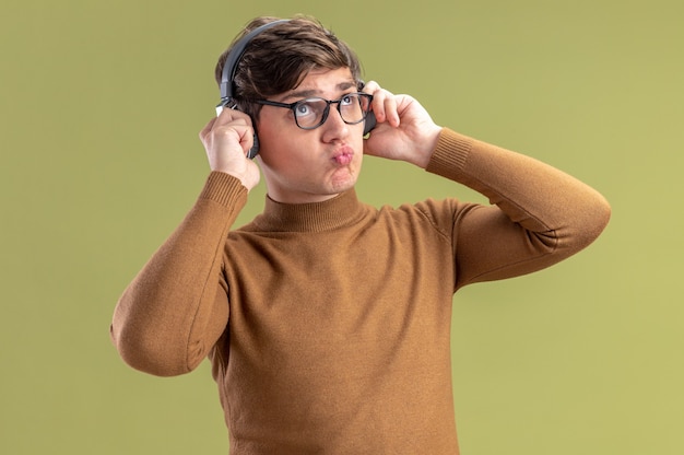 Nachdenklicher junger kaukasischer Junge in optischer Brille und auf Kopfhörern, die nach oben schauen